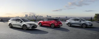 Alle Toyota COROLLA Modelle auf einem Platz mit Blick auf modernes Stadt- und Industriegebiet: Toyota Corolla, Toyota Corolla TS und Corolla Limousine