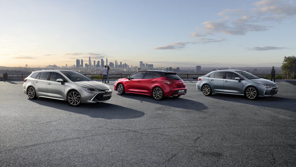 Alle Toyota COROLLA Modelle auf einem Platz mit Blick auf modernes Stadt- und Industriegebiet: Toyota Corolla, Toyota Corolla TS und Corolla Limousine