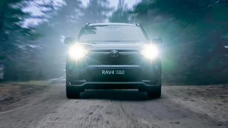 Frontalansicht eines RAV4 Plugin Hybrid auf einer Waldstraße bei trüber Sicht und einsetzender Dunkelheit