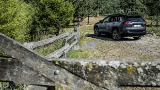 RAV4 Plugin Hybrid im Hintergrund eine Offroad-Umgebung mit Büschen, Steinen und einem alten, verwitterten Holzzaun
