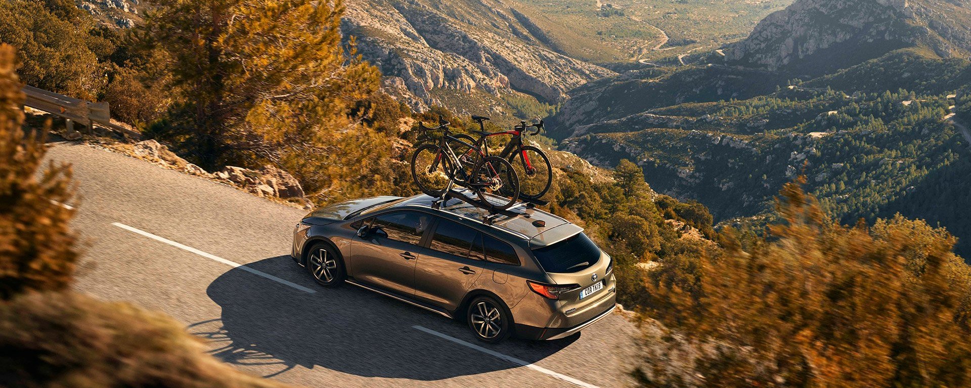 Grauer Toyota auf einer Landstraße in einer bergigen Landschaft von oben fotografiert