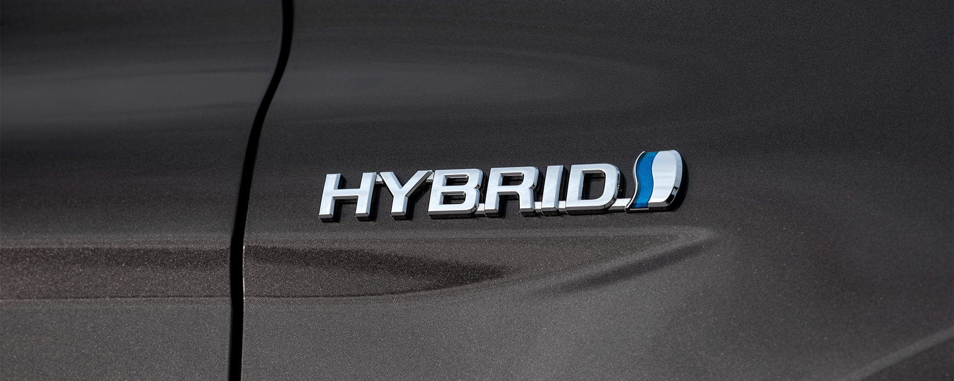 Zu sehen ist eine Nahaufnahme des Wortes HYBRID auf der Seite eines grauen Toyota