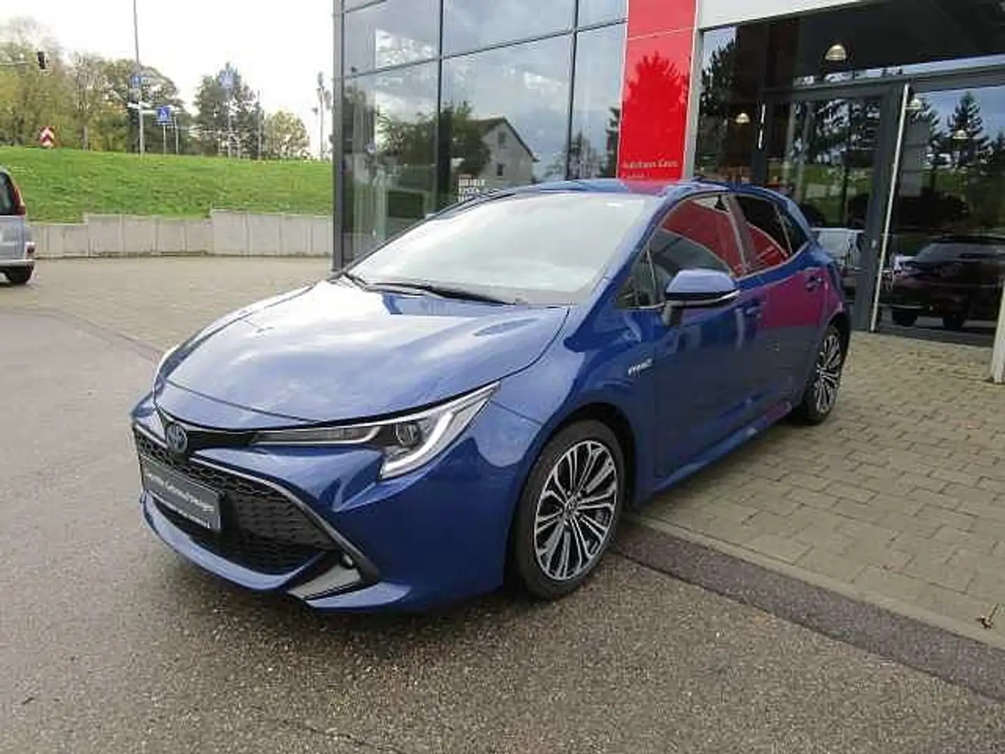 Schrägansicht eines Gebrauchtwagens vor dem Eingang des Autohaus Goos. Bei dem Gebrauchtwagen handelt es sich um einen Corolla mit blauem Lack. Zu sehen ist die linke Vorderseite des Wagens.